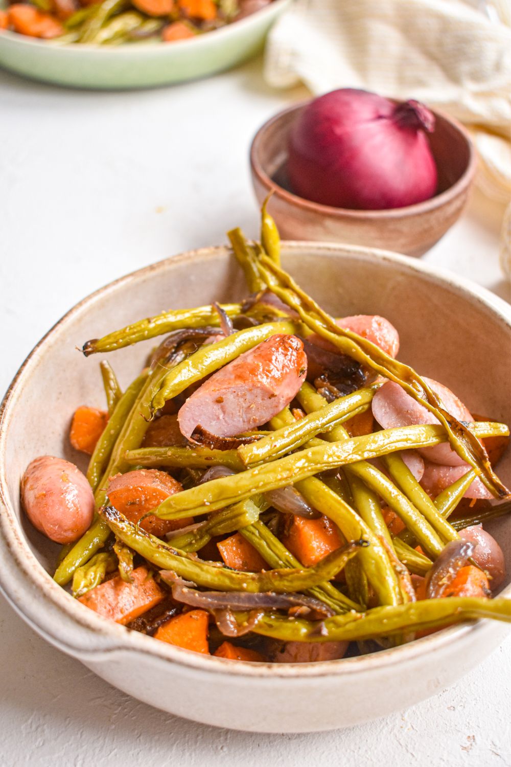 Roasted chicken sausages with chopped sweet potatoes, green beans, and red onion in a bowl with a napkin on the side.