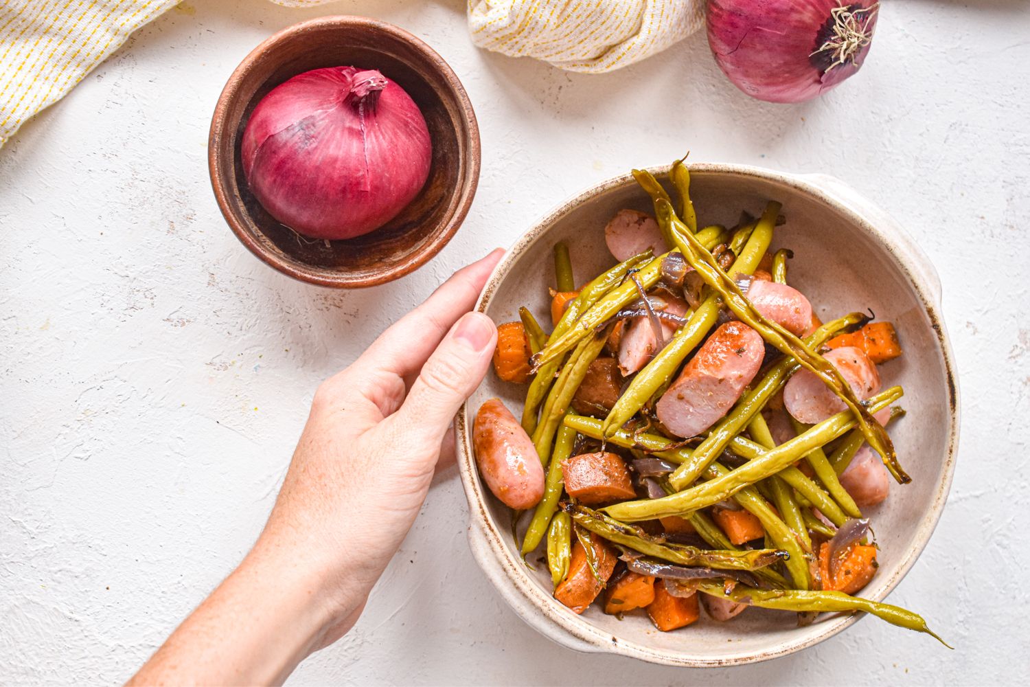 Sheet pan chicken sausage with sweet potatoes and green beans in a bowl being held by a hand.