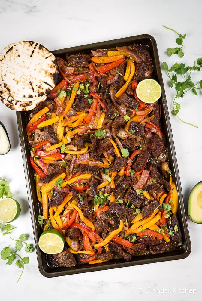 Beef fajitas made on a sheet pan with red onion, bell peppers, lime juice, fajita seasoning, and cilantro served with flour tortillas and avocado.