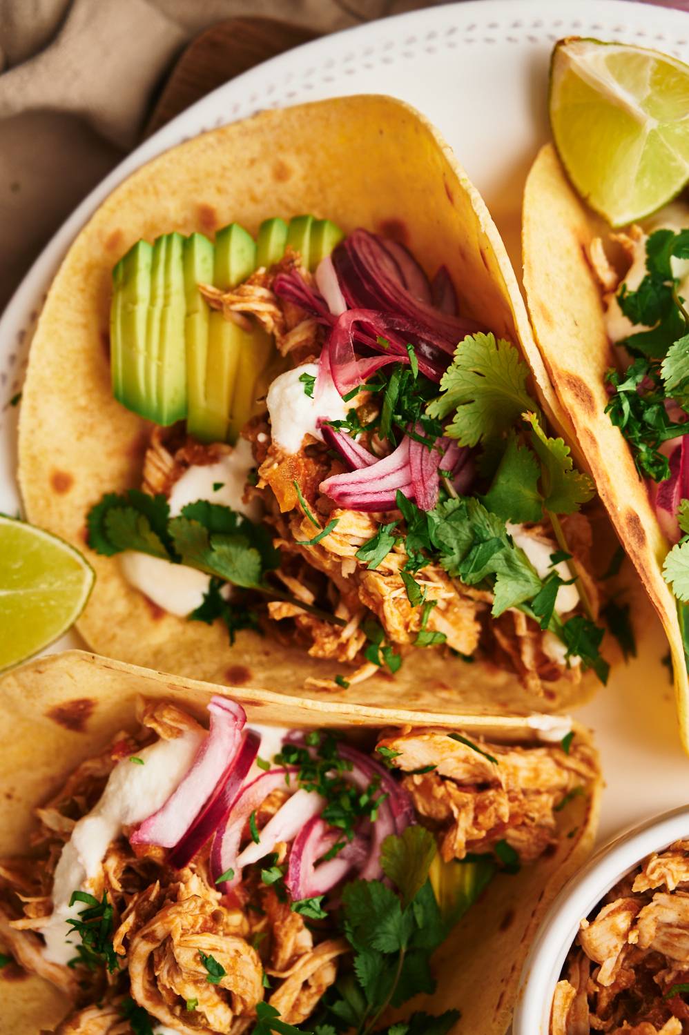 Mexican chicken tacos with shredded chicken, avocado, lime, pickled red onions and corn tortillas on a plate.