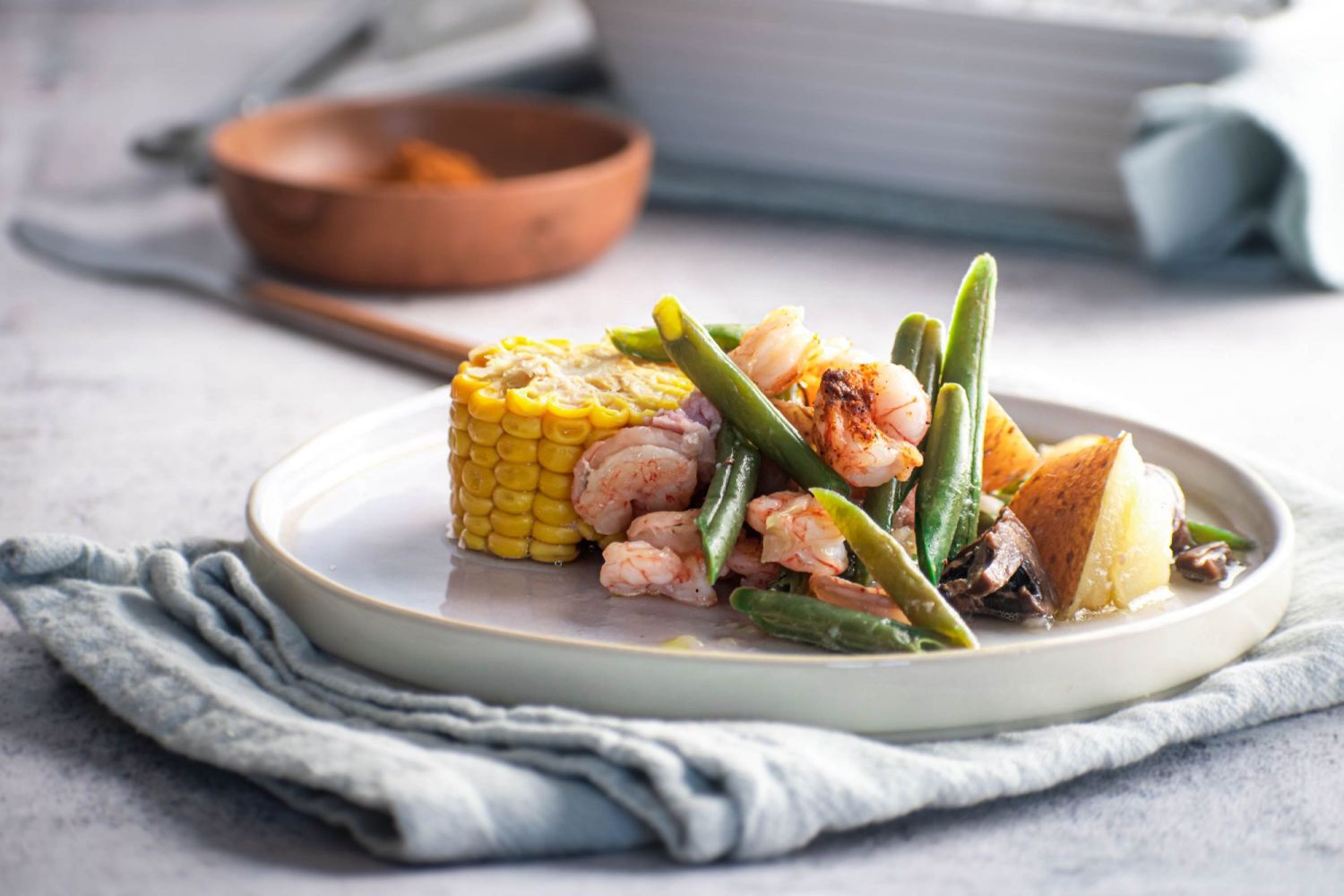 Cajun shrimp, sausage, and corn foil packets with potatoes, green beans, and mushrooms on a plate. 