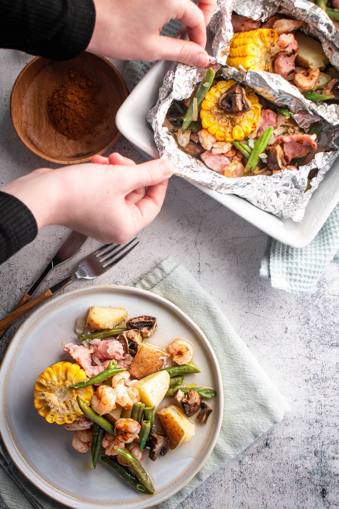 Foil packets with Cajun shrimp boil including corn, shrimp, sausage, green beans, potatoes, and onions.