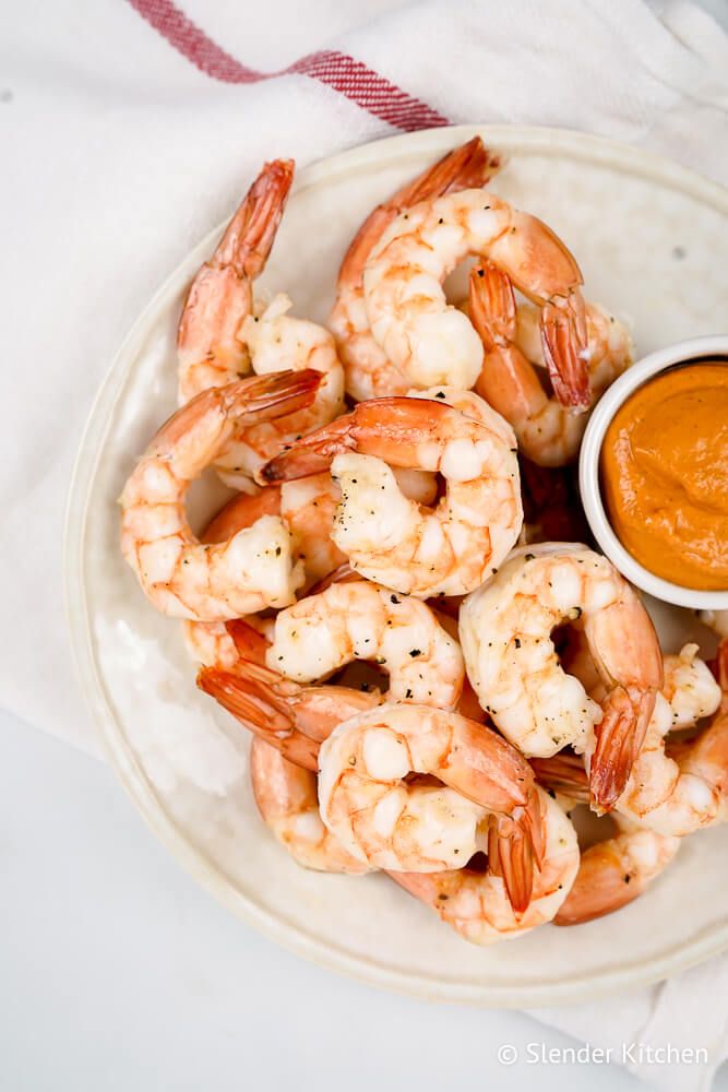 Shrimp cocktail on a white plate with cocktail sauce and a napkin.