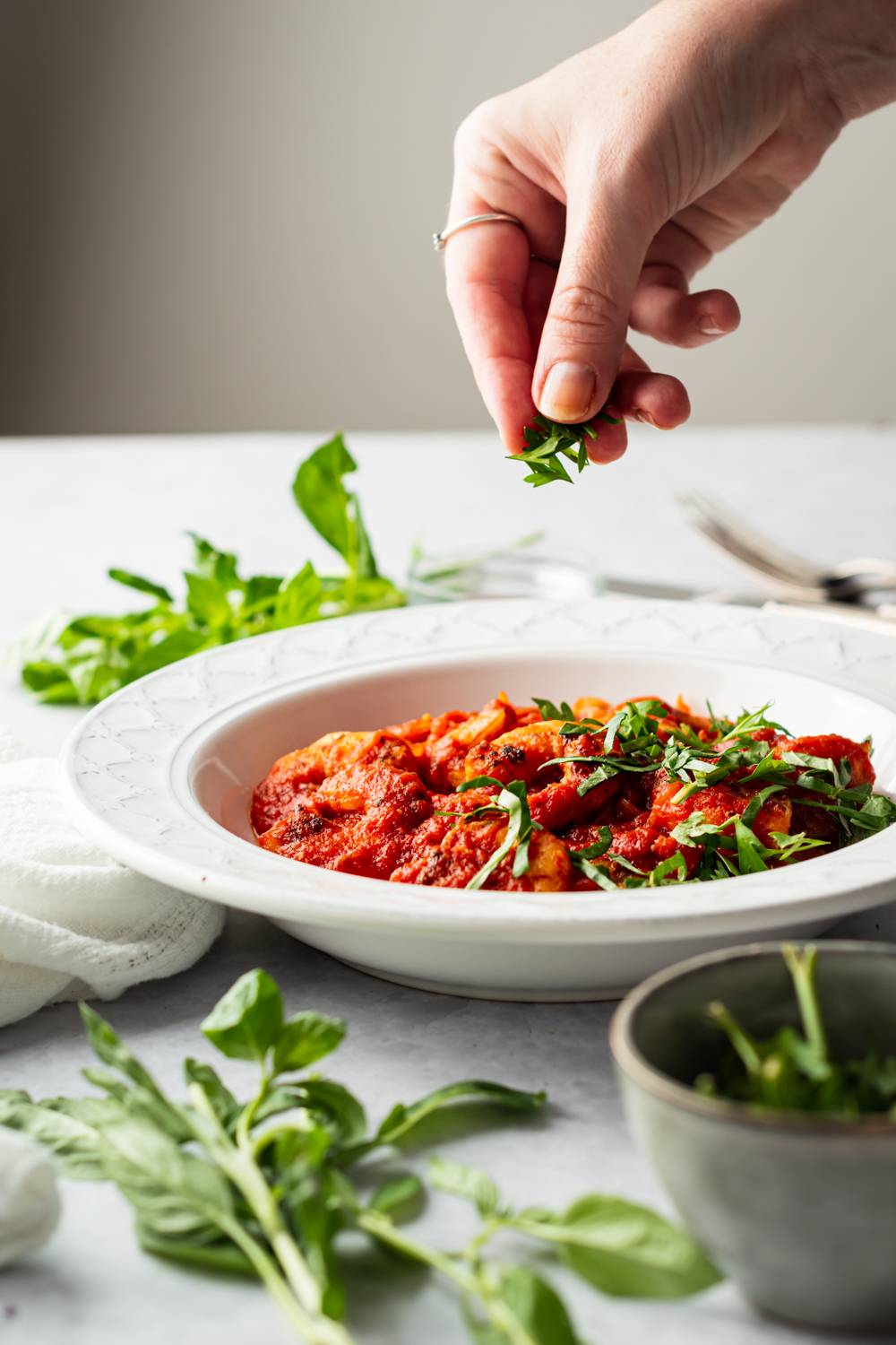 Fresh basil being sprinkled over a bowl of shrimp fra diavolo with cooked shrimp in tomato sauce.