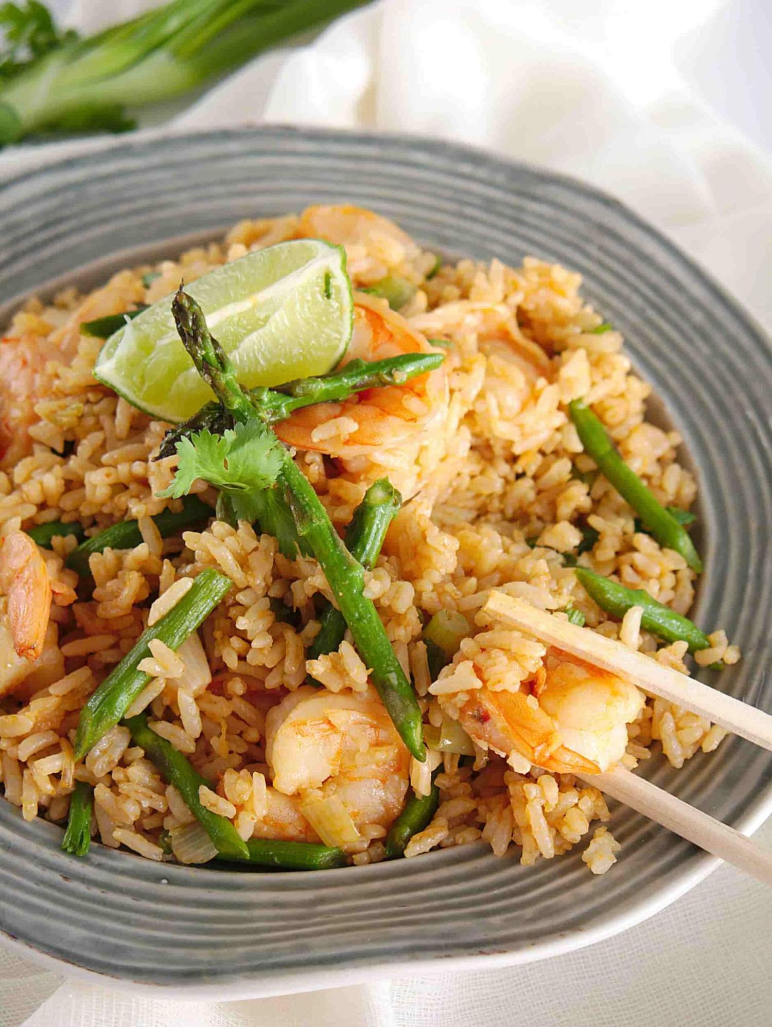 Shrimp fried rice with soy sauce, asparagus, and a lime wedge on a light blue plate.