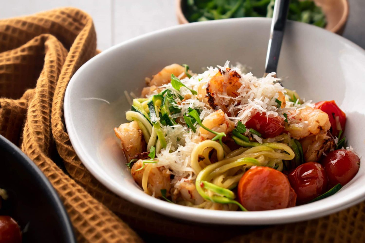 Shrimp scampi zucchini noodles with cherry tomatoes and Parmesan cheese in a white bowl.