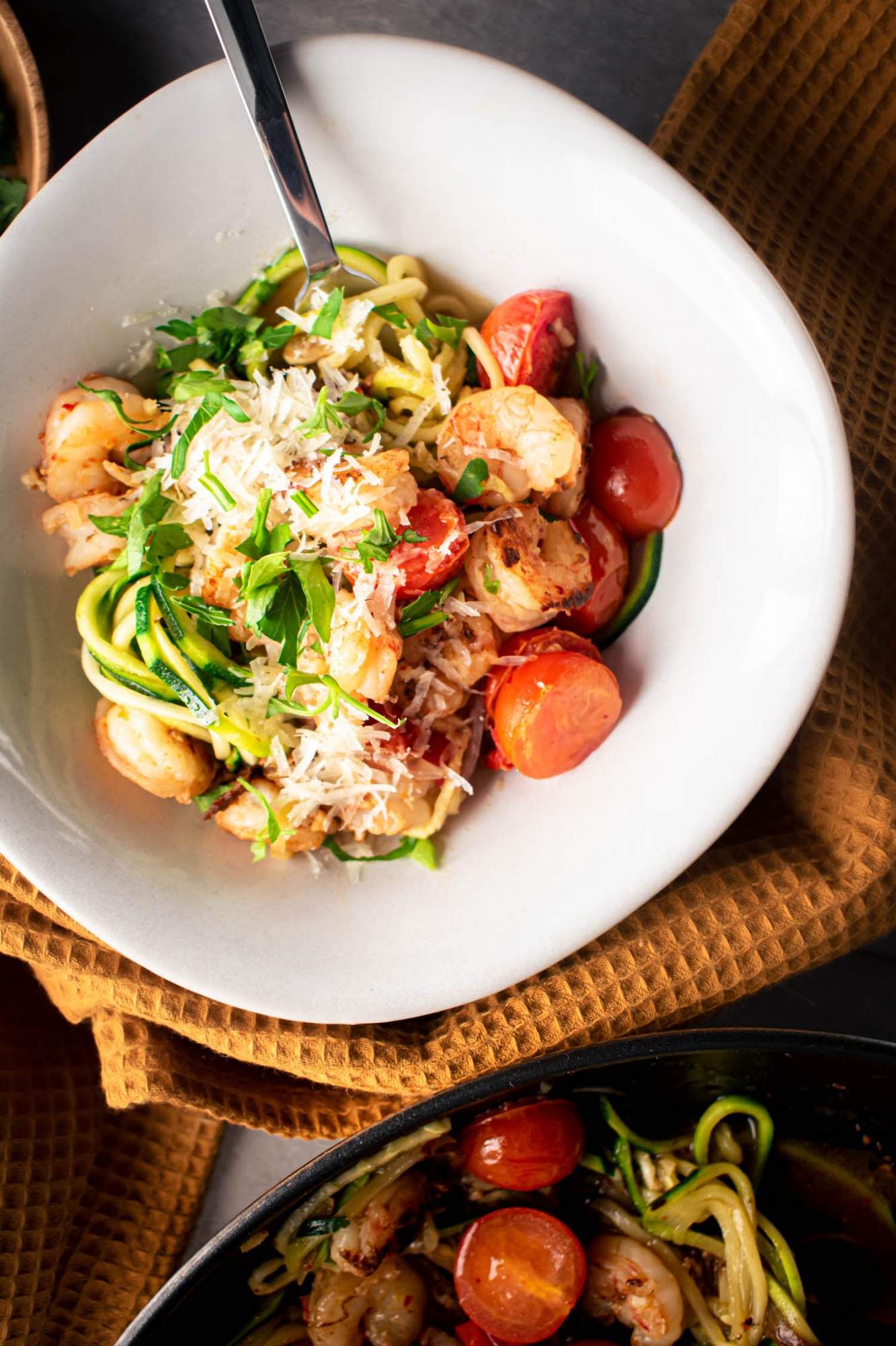 Zucchini noodles with garlic shrimp scampi in a bowl with fresh Parmesan cheese and parsley.