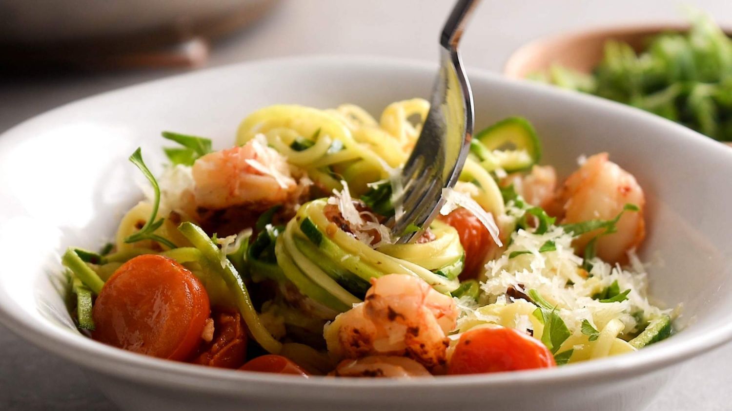 Zoodles with shrimp scampi and tomatoes being twirled around a fork in a bowl.