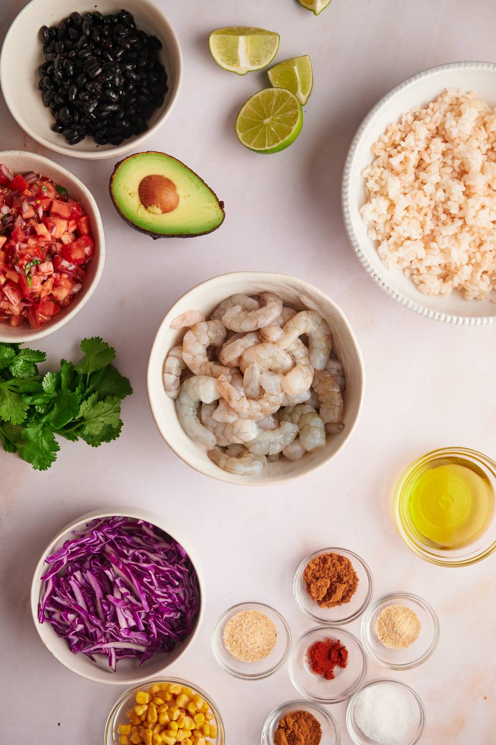 Ingredients for shrimp taco bowls including raw shrimp, rice, black beans, cabbage, lime, and pico de gallo.