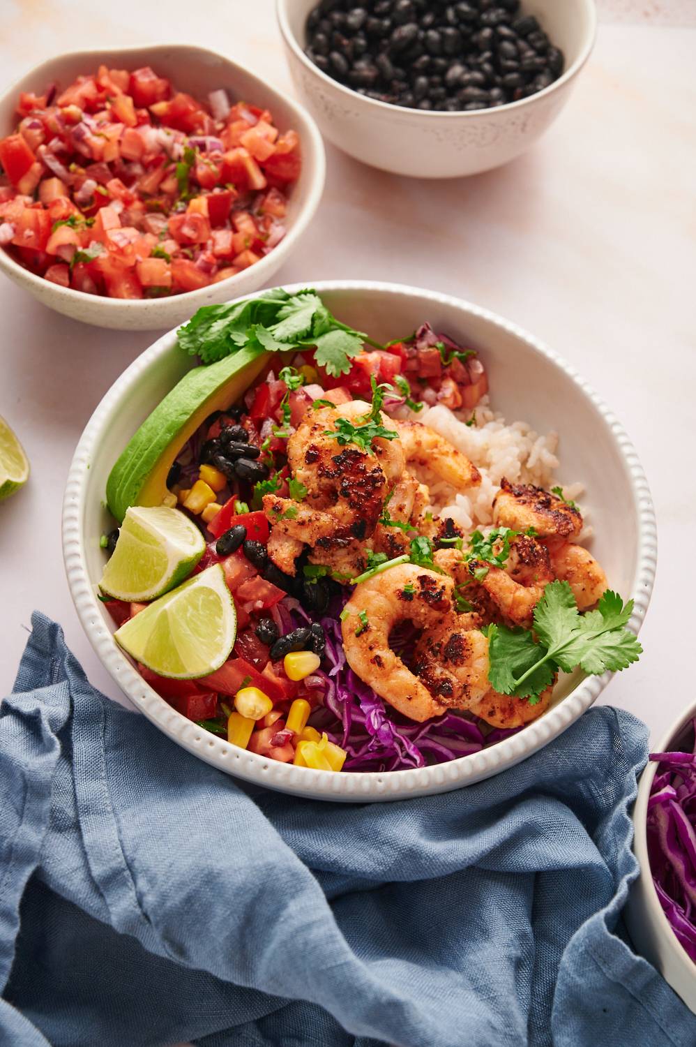 Taco bowls with seasoned shrimp, salsa, avocado, beans, corn, and rice served with lime and cilantro.