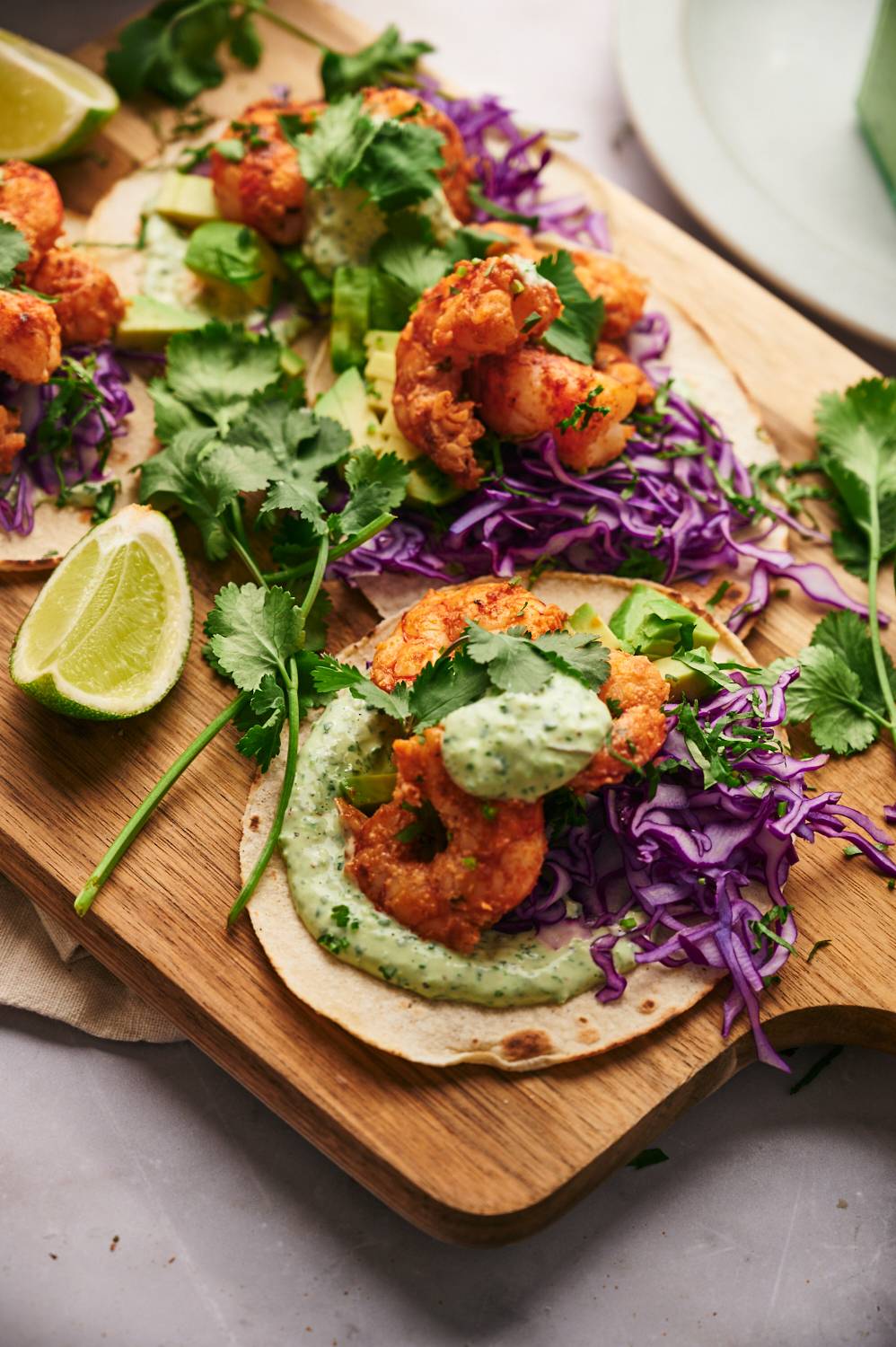 Homemade shrimp tacos served on a wooden board with lime wedges, cilantro, avocado, and purple cabbage.