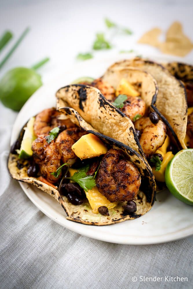 Shrimp tacos with mango salsa and black beans in corn tortillas with limes and green onions.