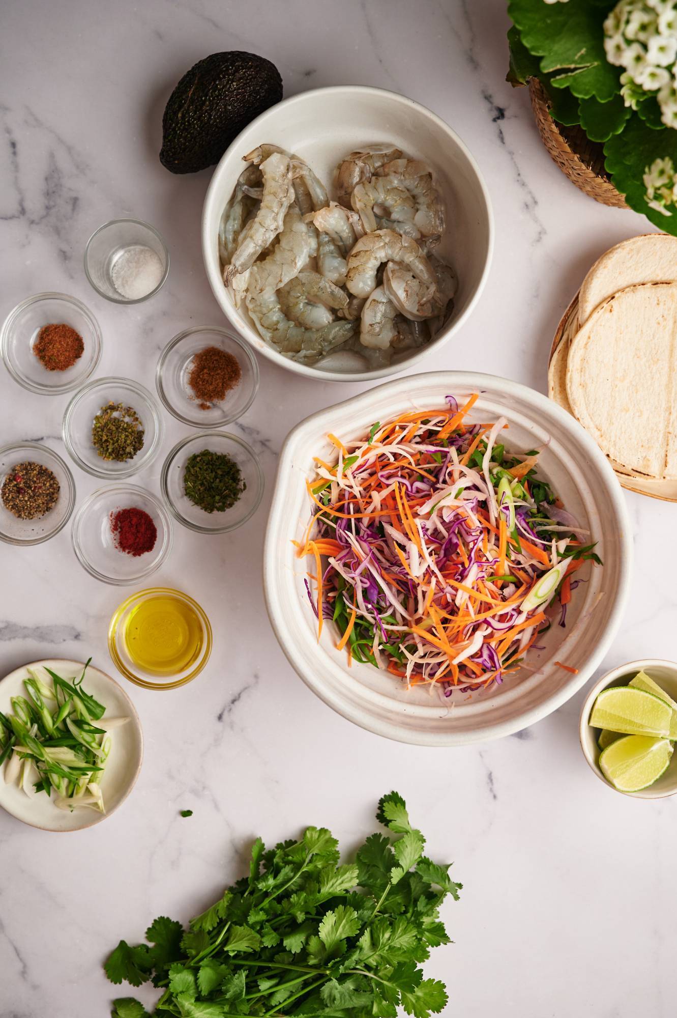 Ingredients for shrimp tacos with slaw including raw shrimp, spices, olive oil, and shredded cabbage. 