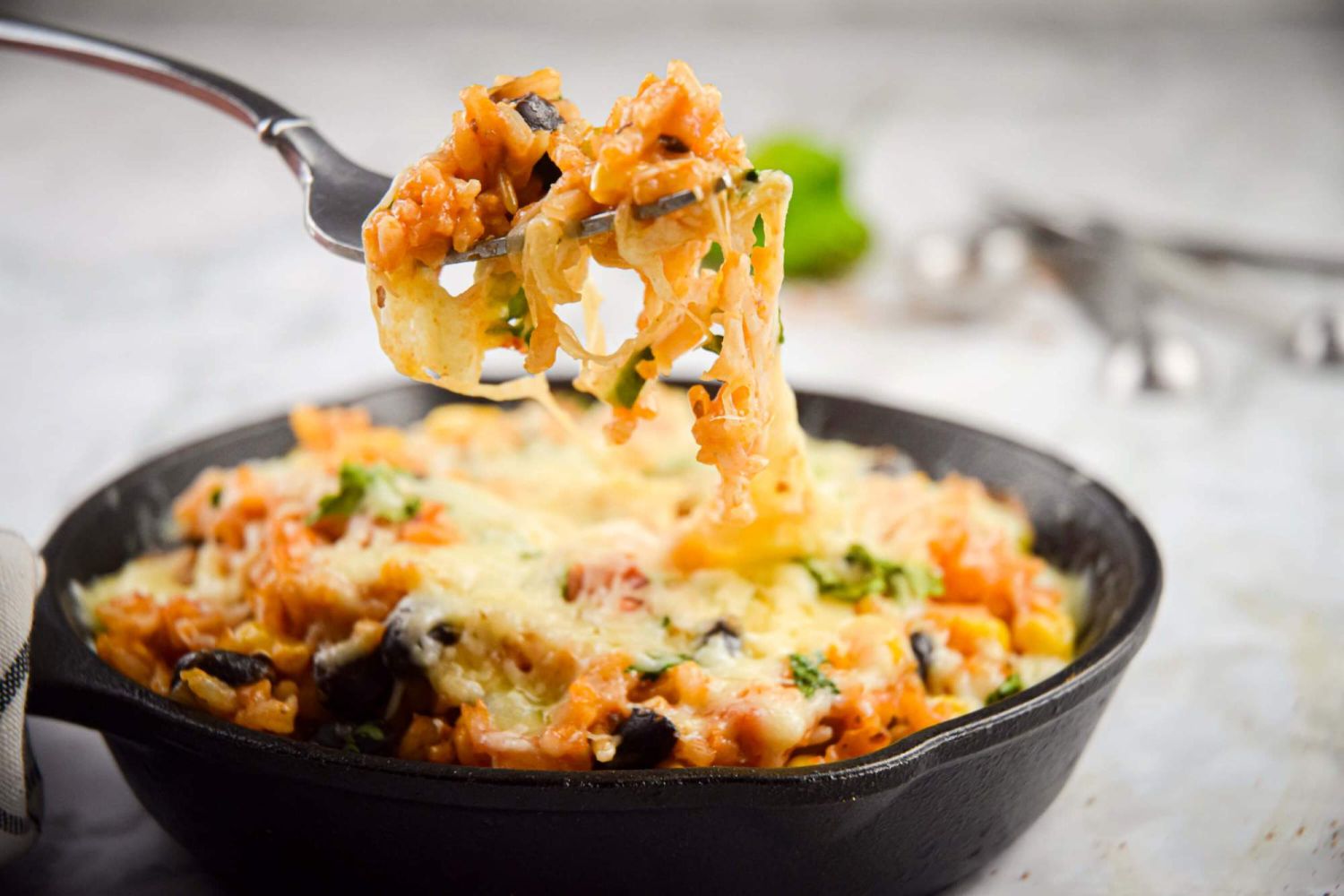 Mexican brown rice skillet with black beans, vegetables, corn, and taco seasoning in a skillet being eaten with a fork.