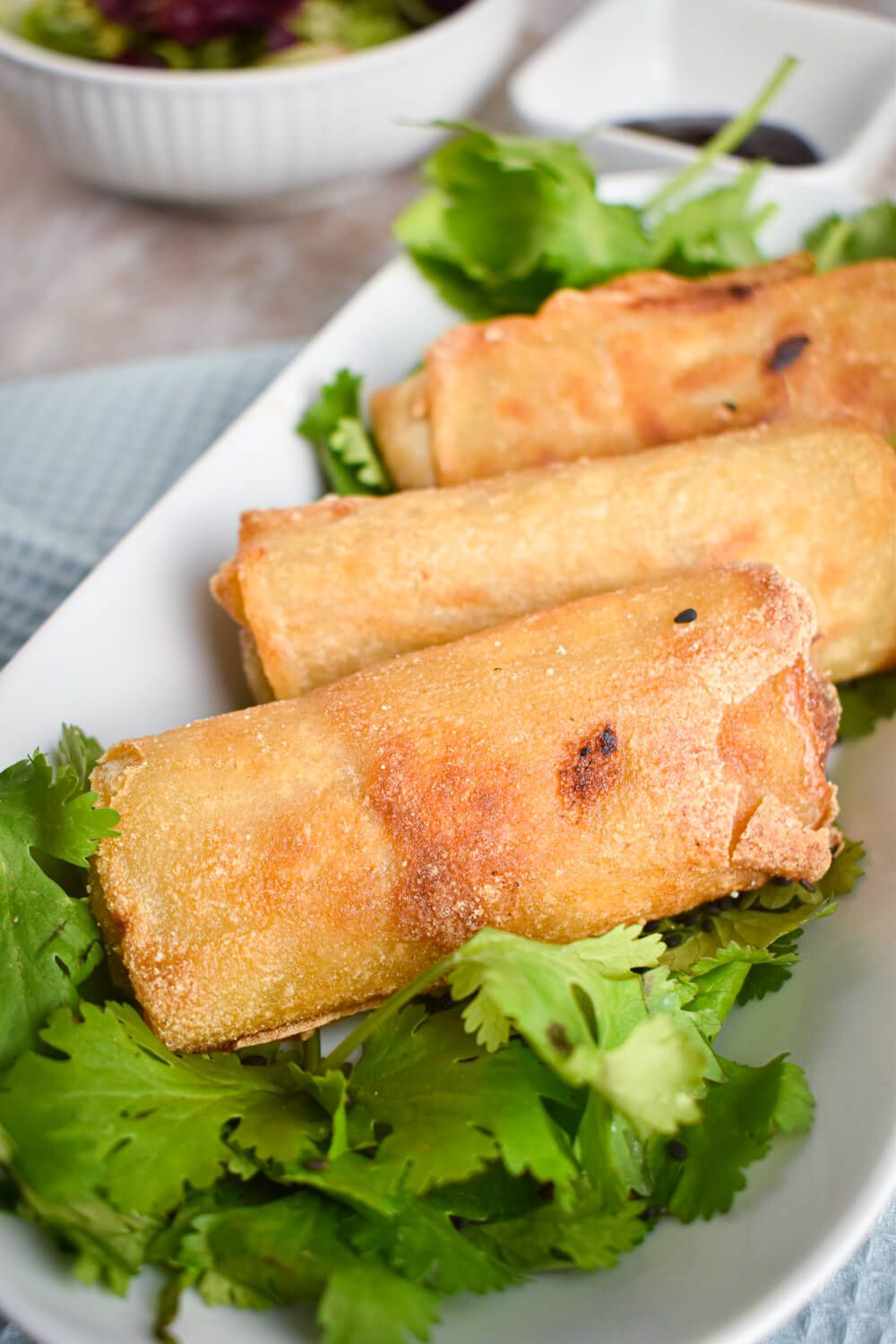 Egg rolls with a crispy brown exterior on a plate with cilantro.