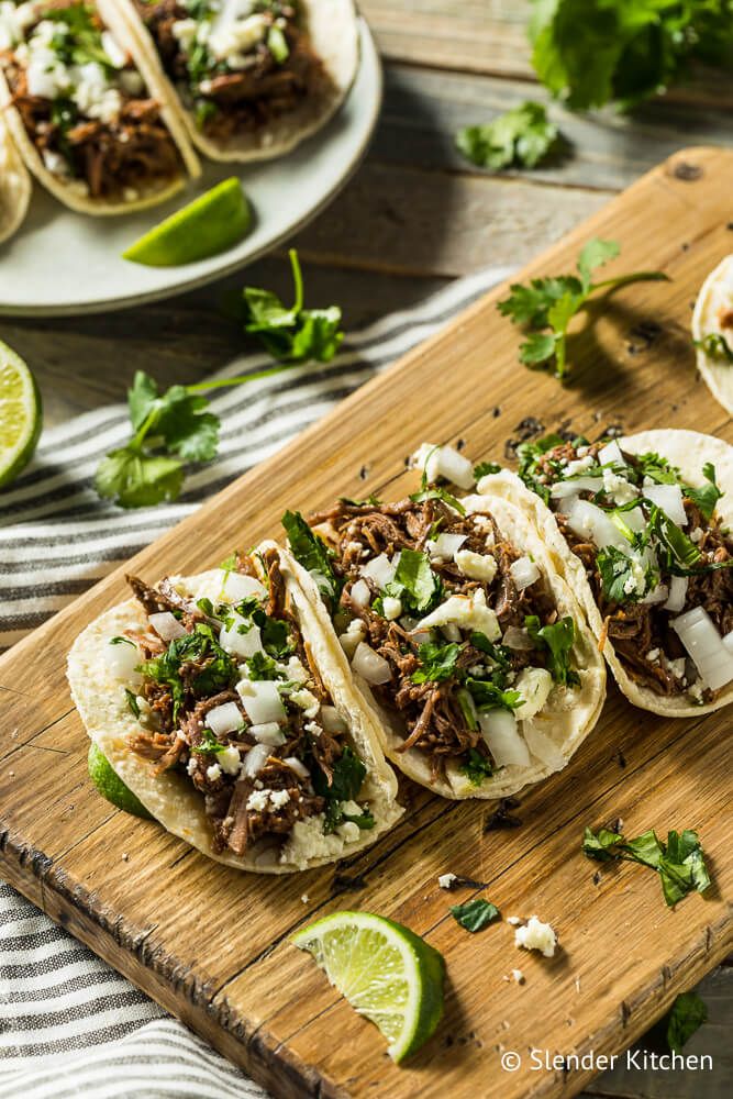 Beef barbacoa tacos with onion, cilantro, and queso fresco in corn tortillas with limes.