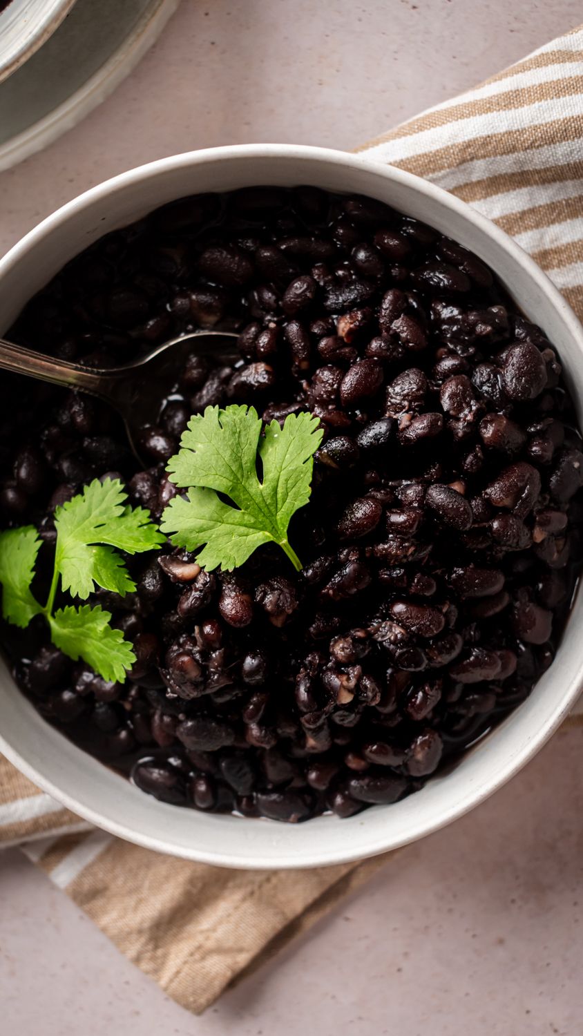 Crockpot black beans in a rich broth in a bowl with fresh cilantro leaves.