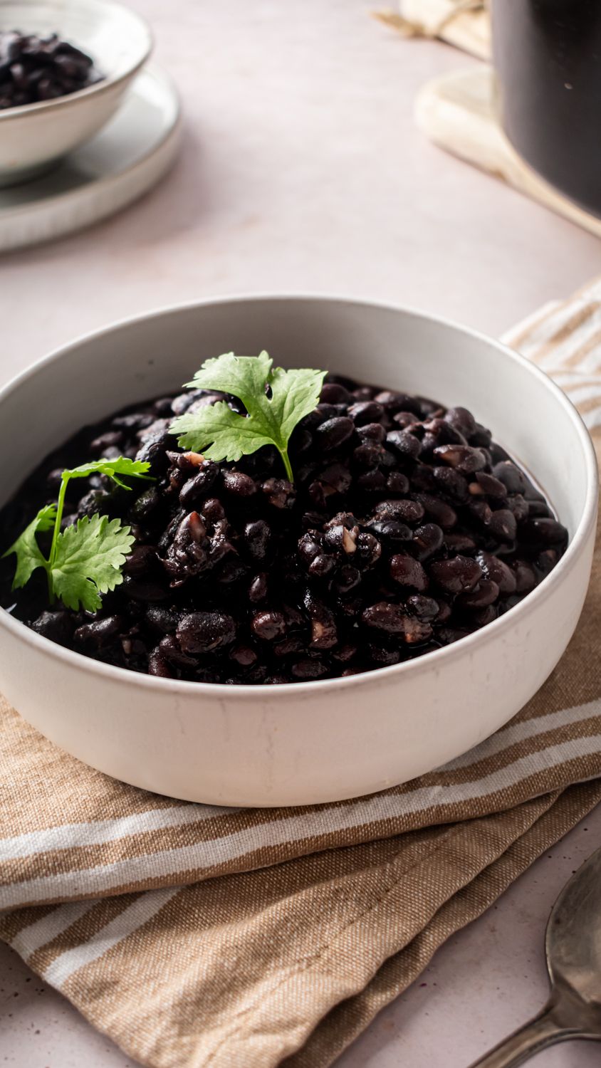 Cooked black beans with onion, garlic, and spices in a white bowl served on a brown napkin. 