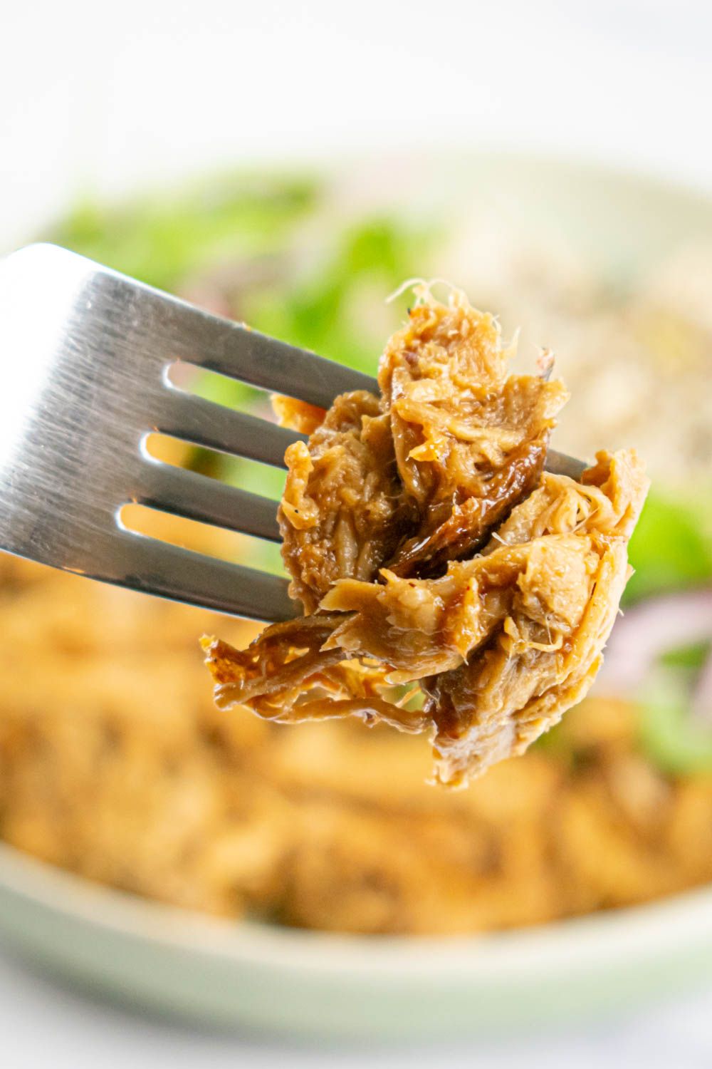 Char Sui Pork on a fork with Chinese barbecue sauce and a blurred bowl in the background.