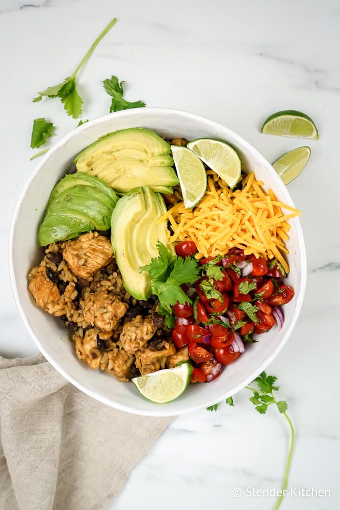 Slow cooker burrito bowls with chicken, beans, rice, avocado, cheese, and vegetables in a bowl.