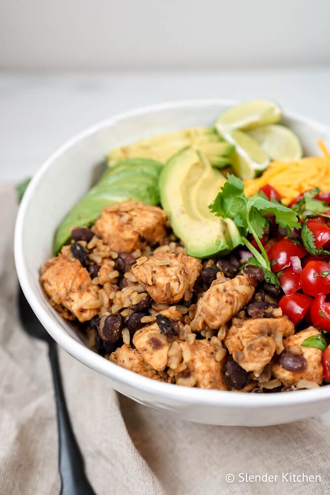 Crockpot chicken burrito bowls with rice, chicken, black beans, tomatoes, cilantro, avocado, and cheese.