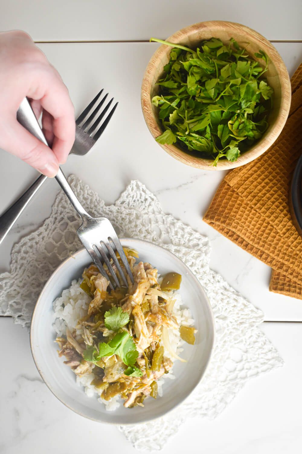 Crockpot chicken chile verde in a bowl with cilantro, white rice, and a fork.