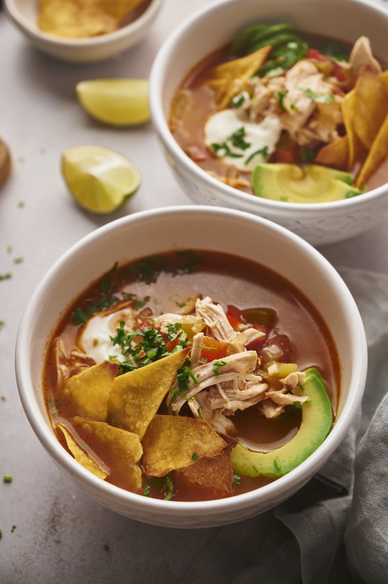 Chicken fajita soup with bell peppers and onions in a bowl with tomato broth, avocado, sour cream, and chips.