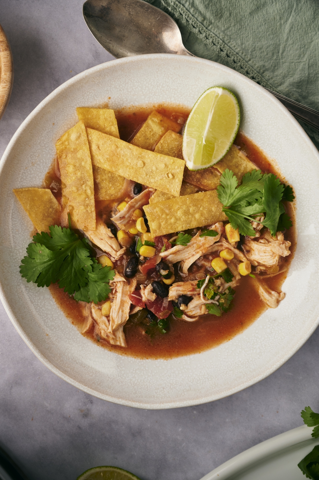 Crockpot chicken tortilla soup with crispy tortillas, chicken, beans, and corn in a bowl with tomato broth.