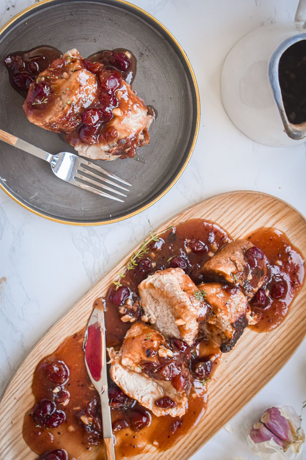 Crockpot cranberry pork sliced on a plate with cranberry sauce and fresh herbs.