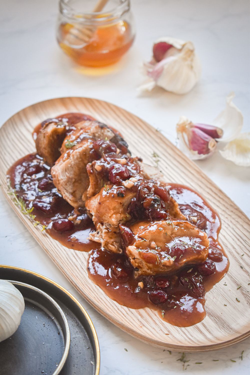 Cranberry pork roast that was cooked in the slow cooker on a wooden plate with garlic and honey on the side.