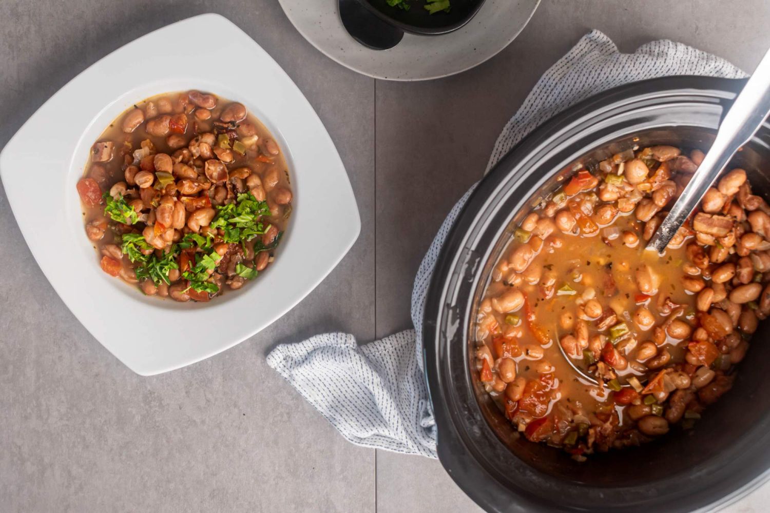 Crockpot charro beans in a bowl with Mexican pinto beans, onions, jalapenos, and spices with a slow cooker on the side.