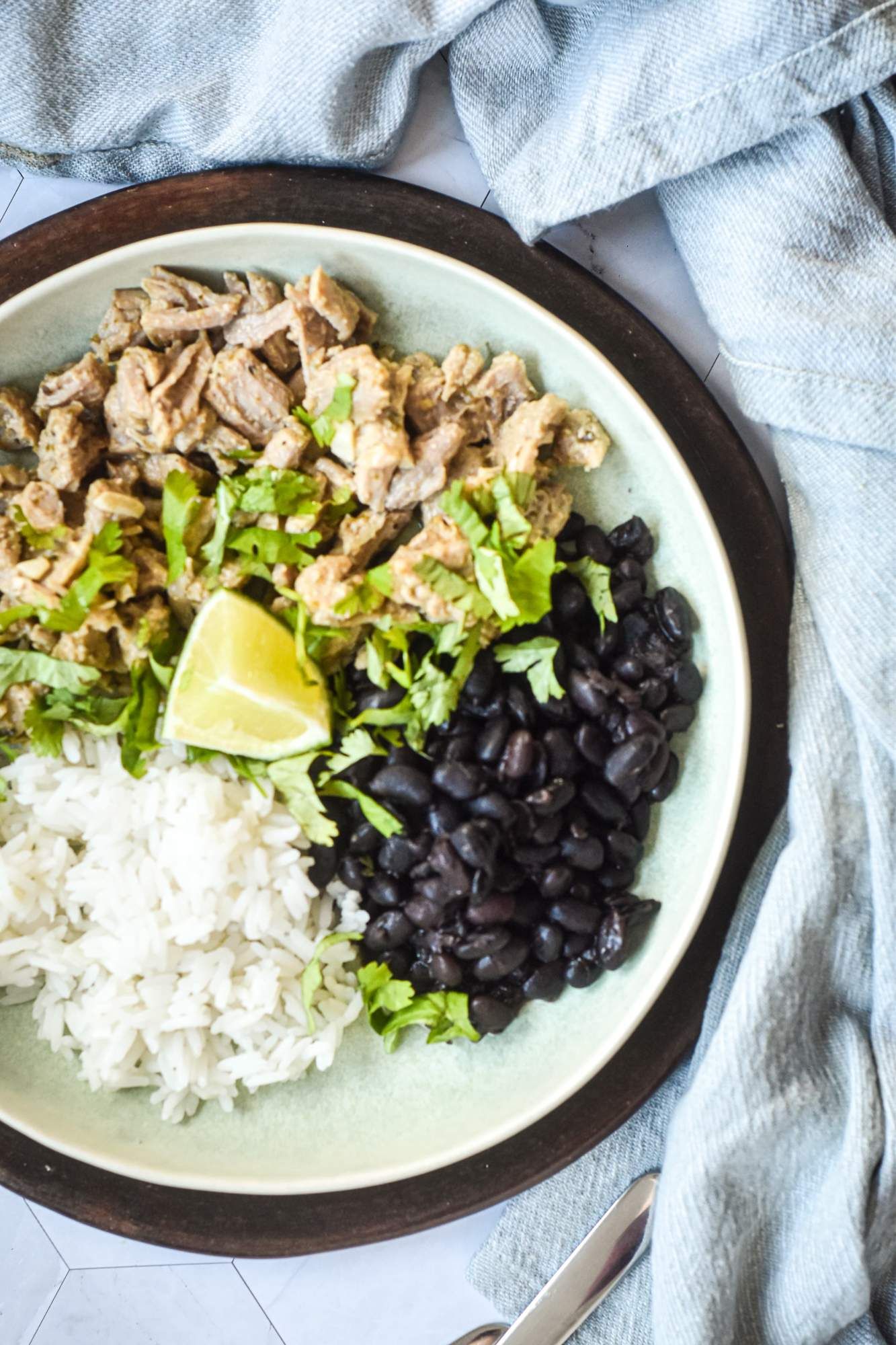 Cuban pork with orange juice and lime juice shredded on a plate with black beans and white rice.