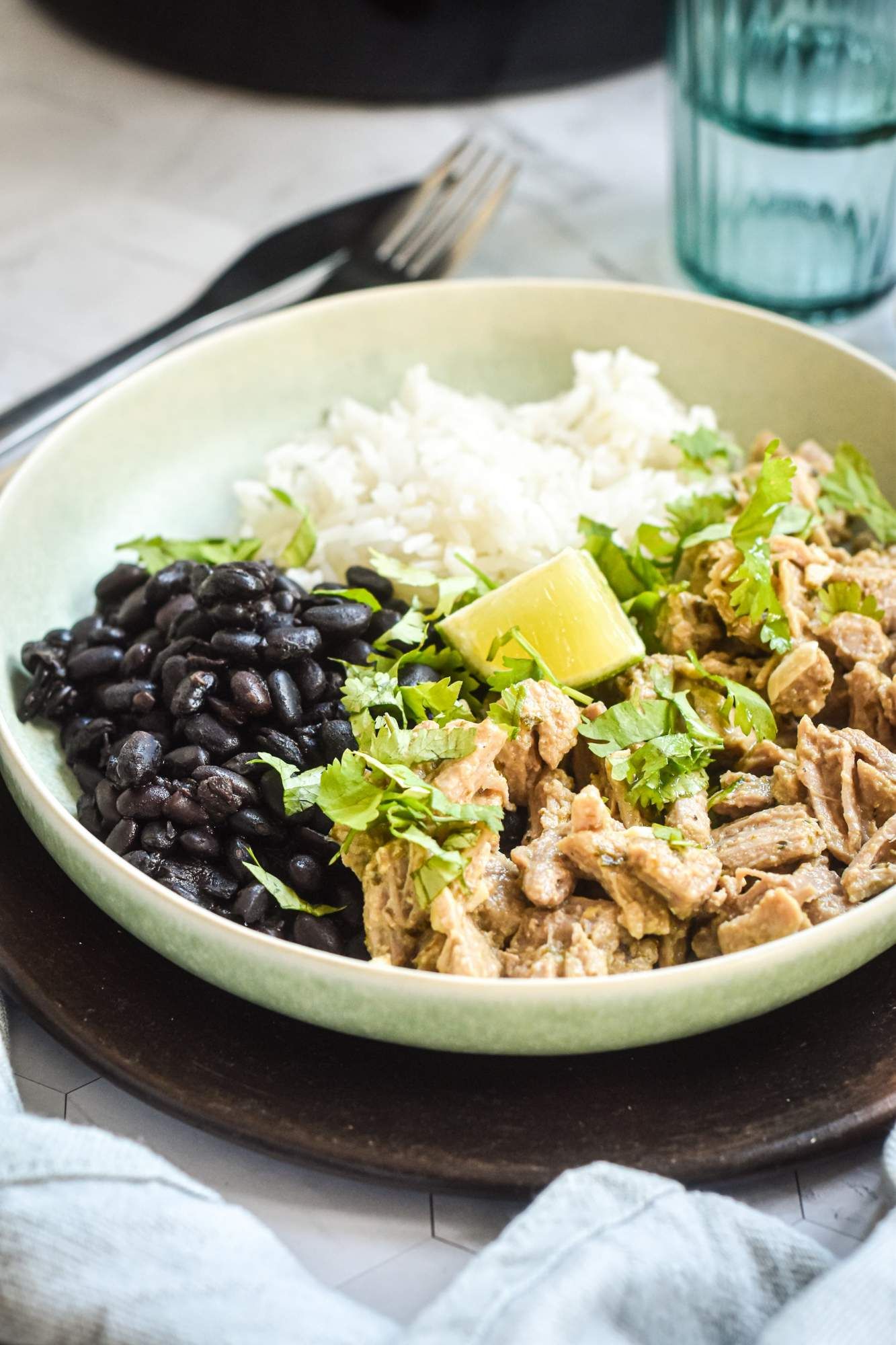 Crockpot shredded Cuban pork with cilantro, fresh limes, white rice, and black beans on a plate. 