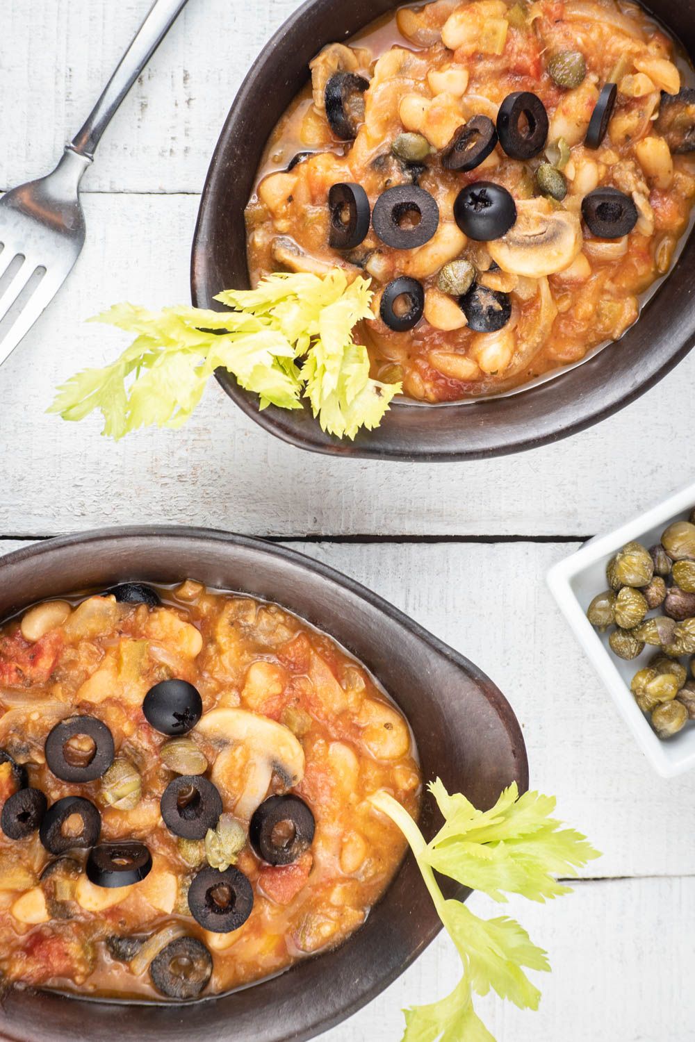 Slow Cooker Italian Beans in two bowls with olives, capers, and celery in tomato sauce.