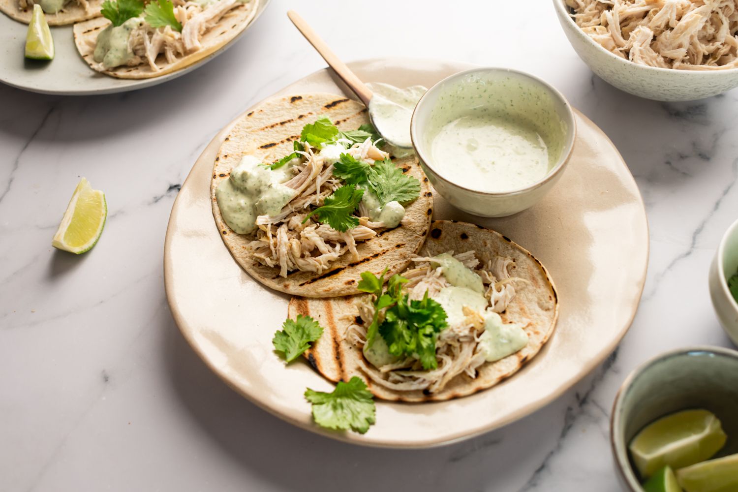 Chicken tacos with jalapenos and a creamy cilantro sauce made with yogurt and limes on a plate with corn tortillas.