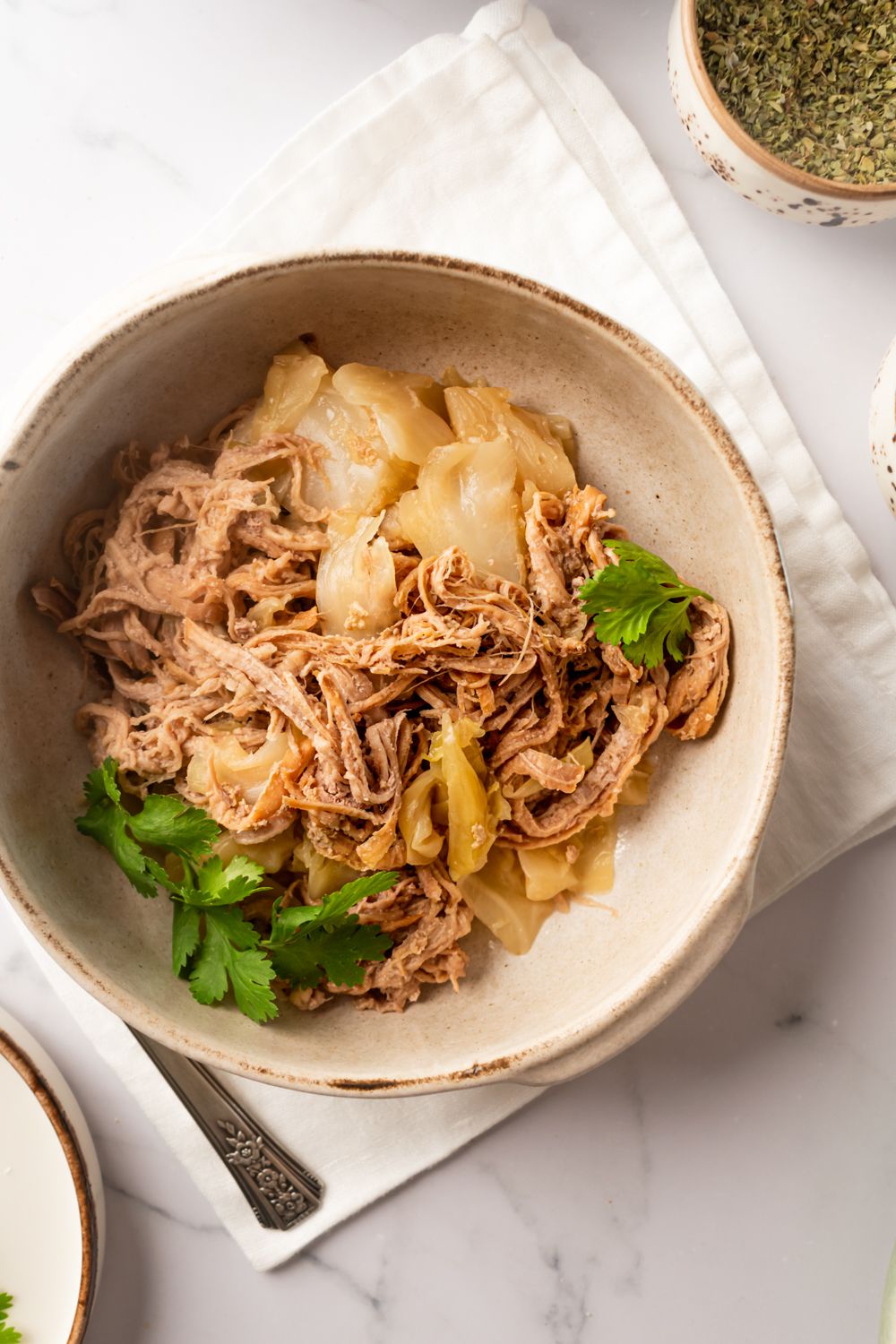 Kalua pork cooked in the slow cooker with green cabbage served in a bowl with Hawaiian salt on the side.