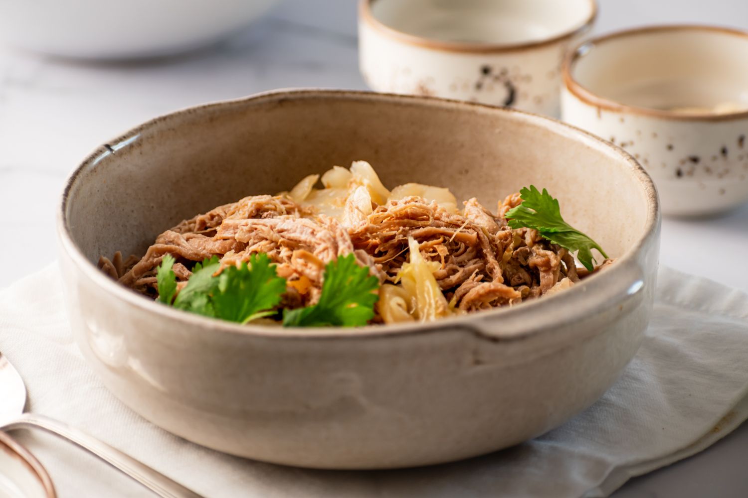 Hawaiian pork with cabbage, liquid smoke, and Hawaiian sea salt in a ceramic bowl with fresh cilantro leaves.