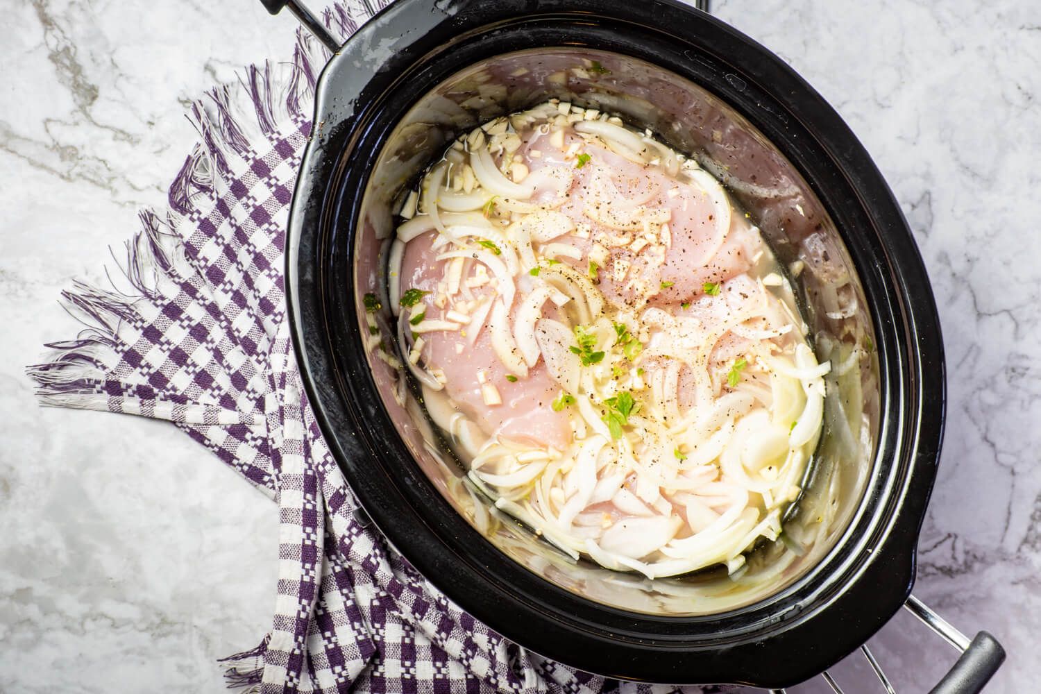 Crockpot lemon garlic chicken in a black slow cooker with onions and garlic.