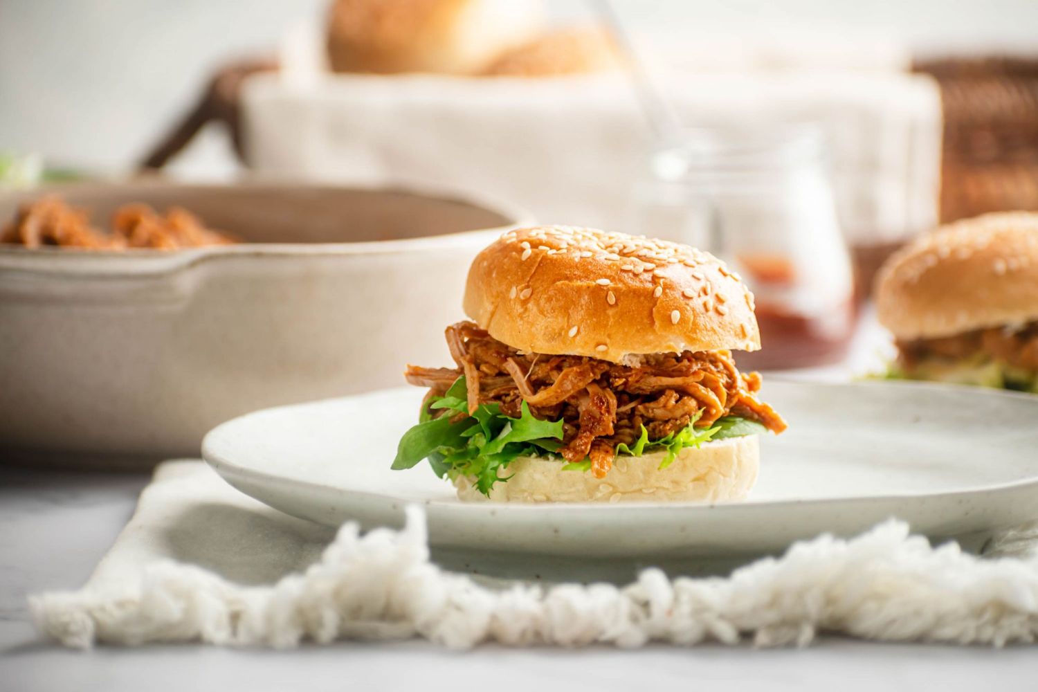 Spicy pulled pork sandwich on a sesame seed bun with lettuce.