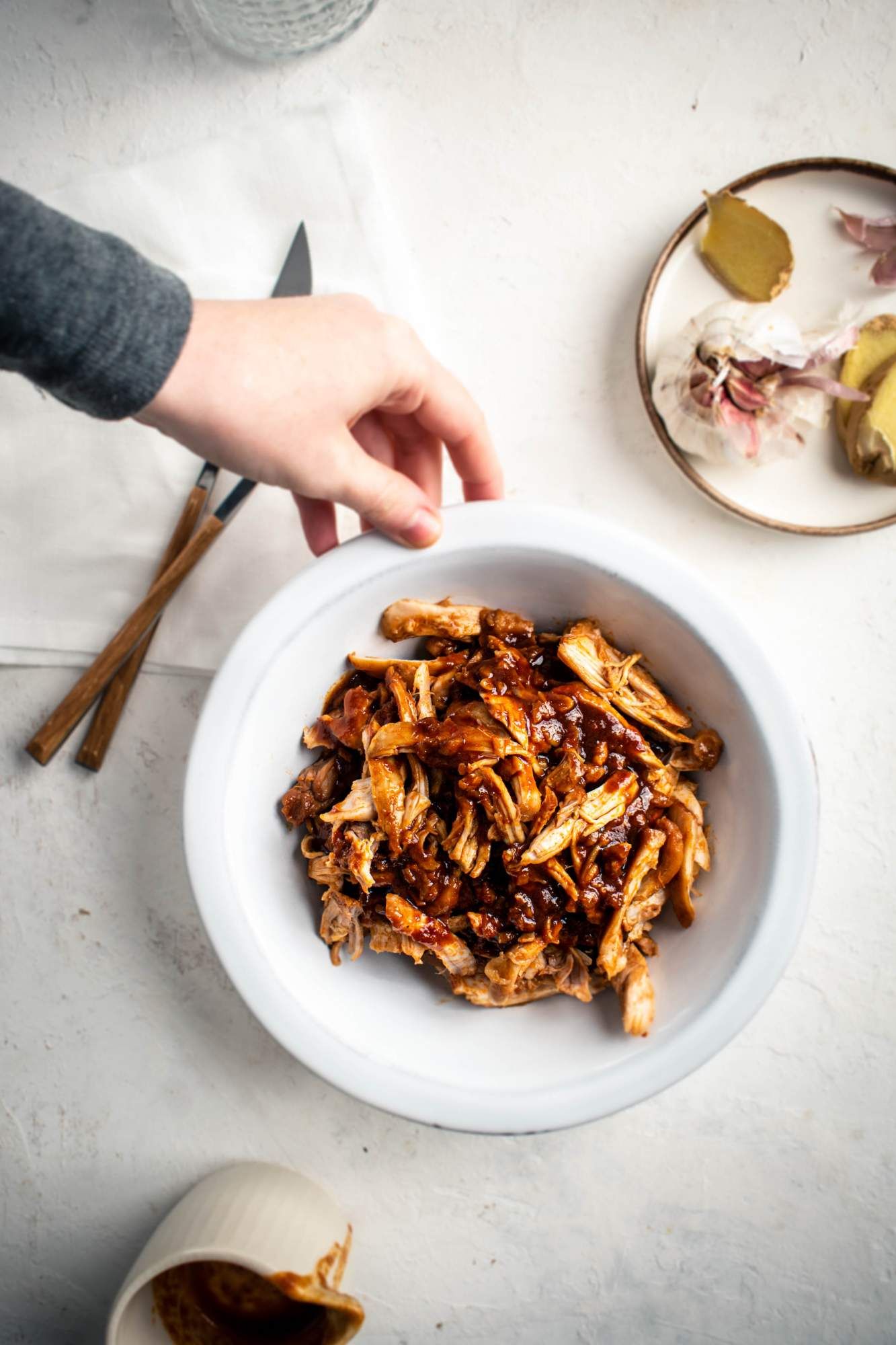 Asian sweet and spicy chicken shredded in a bowl with garlic and ginger on the side.