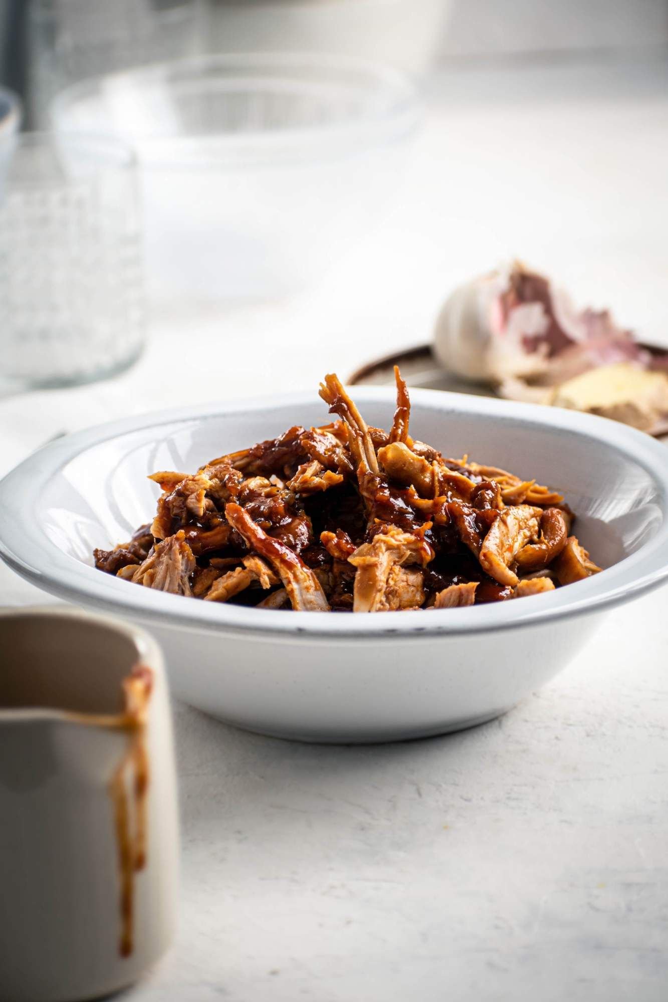 Shredded chicken in a sweet and spicy sauce in a bowl with sambal olek, garlic, and soy sauce.