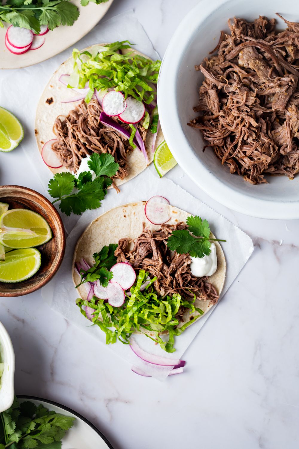 Tri tip tacos  made in the slow cooker served on tortillas with cilantro, lime, lettuce, red onions, and radish slices.