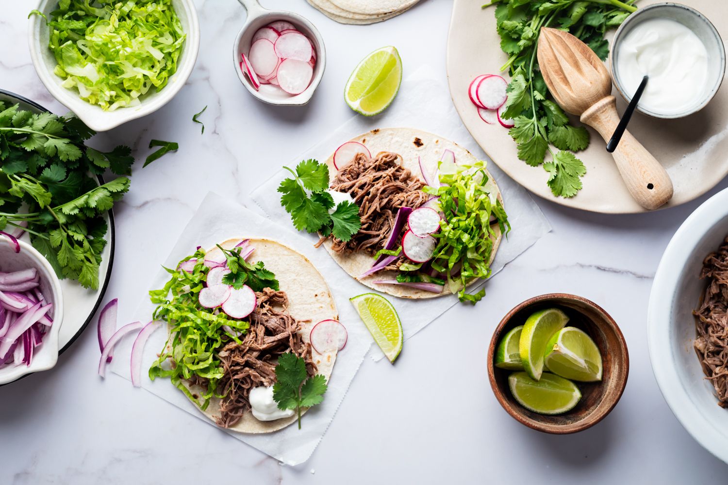 Crockpot tri-tip shredded tacos with red onion, cilantro, lettuce, and radishes served on corn tortillas.