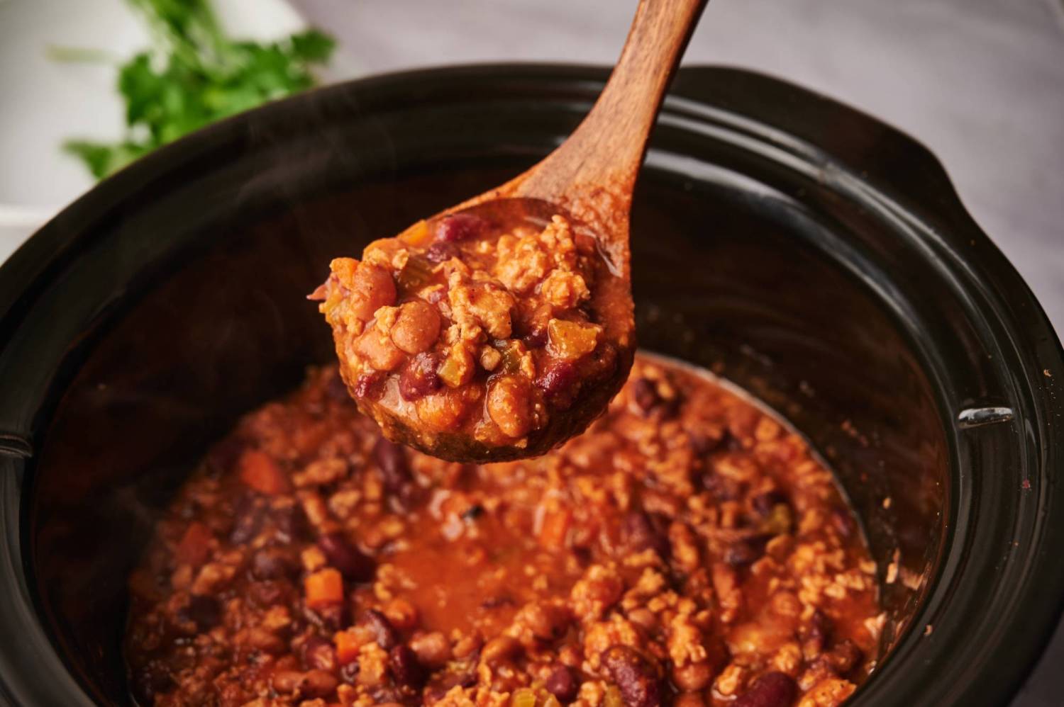 Turkey chili in a wooden spoon with pinto beans, kidney beans, and ground turkey.