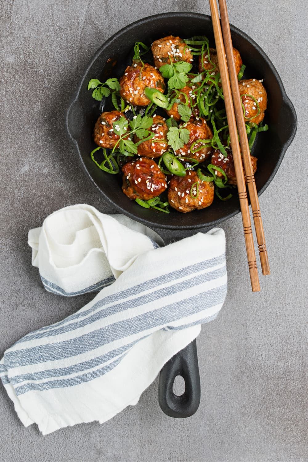 Crockpot vegetarian Asian meatballs in a cast iron skillet with hoisin sauce, green onions, cilantro, and sliced jalapenos.