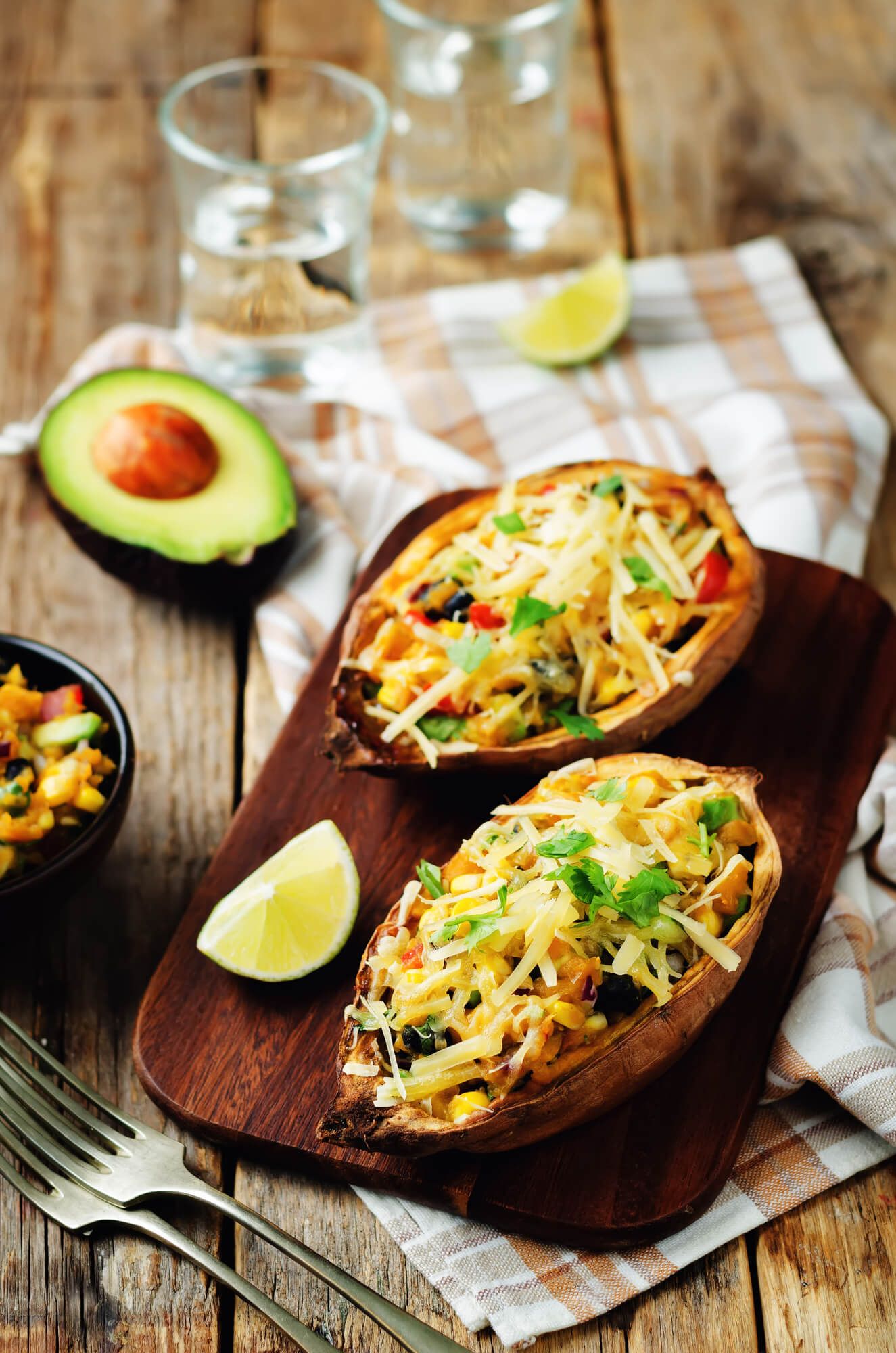 Two baked stuffed sweet potatoes with black beans, corn, melted cheese, and tomatoes.