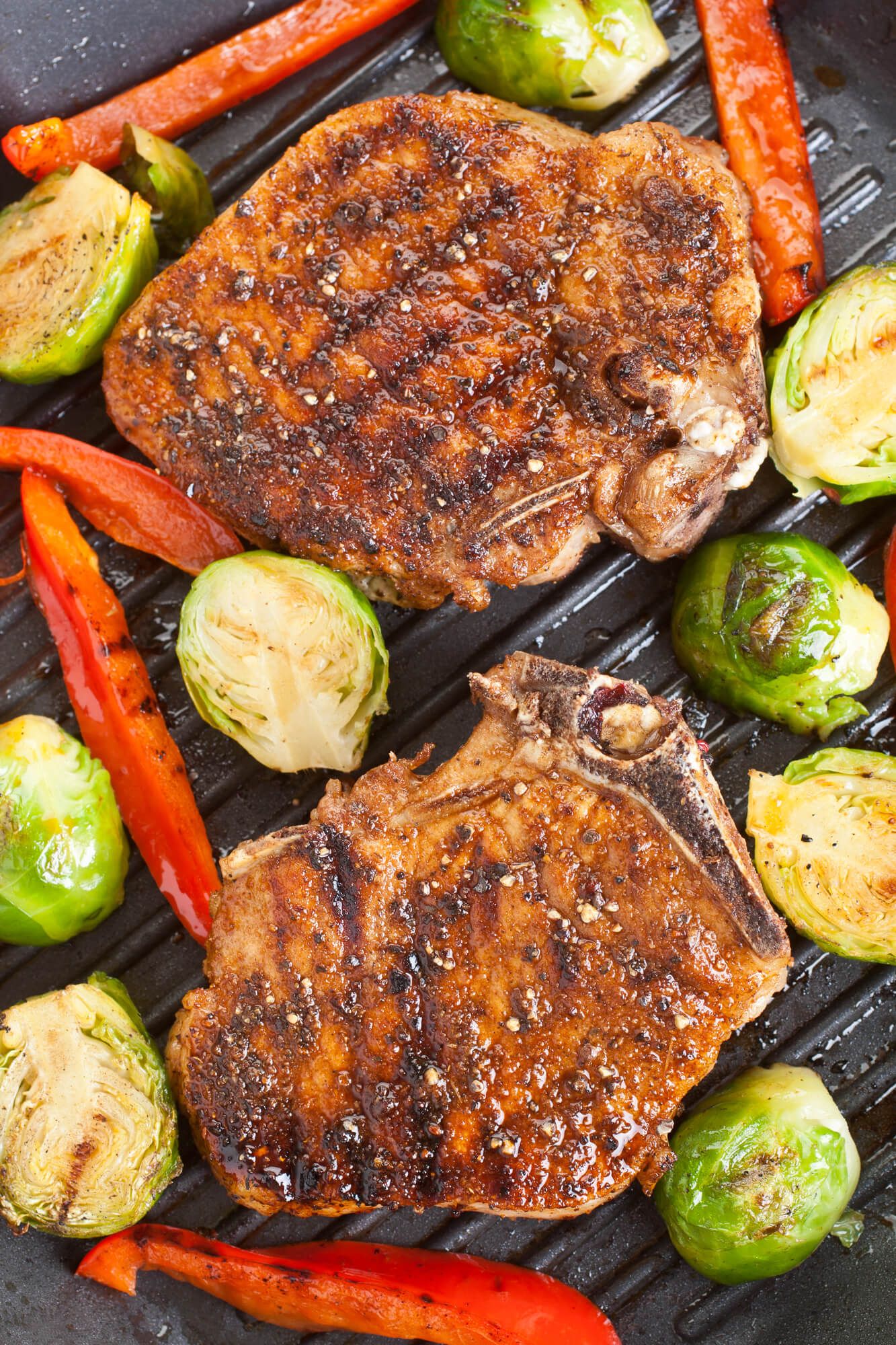 Grilled Pork Chops with peppers and Brusslels sprouts on a grill pan.