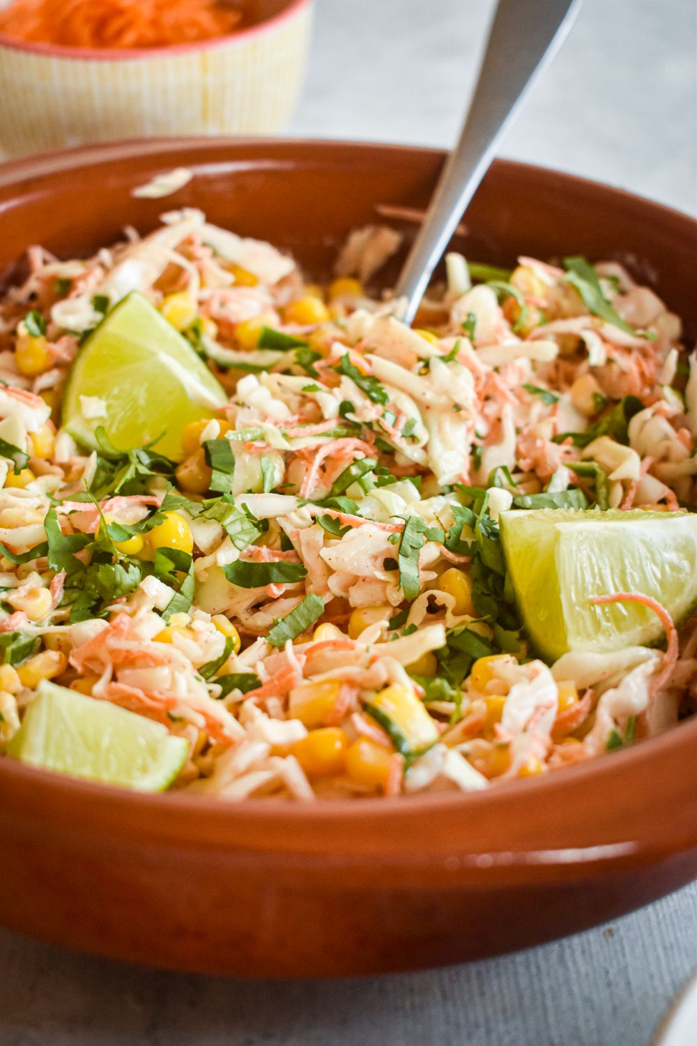 Cabbage and corn slaw with a spicy dressing in a wooden bowl with shredded carrots, cabbage, and corn.