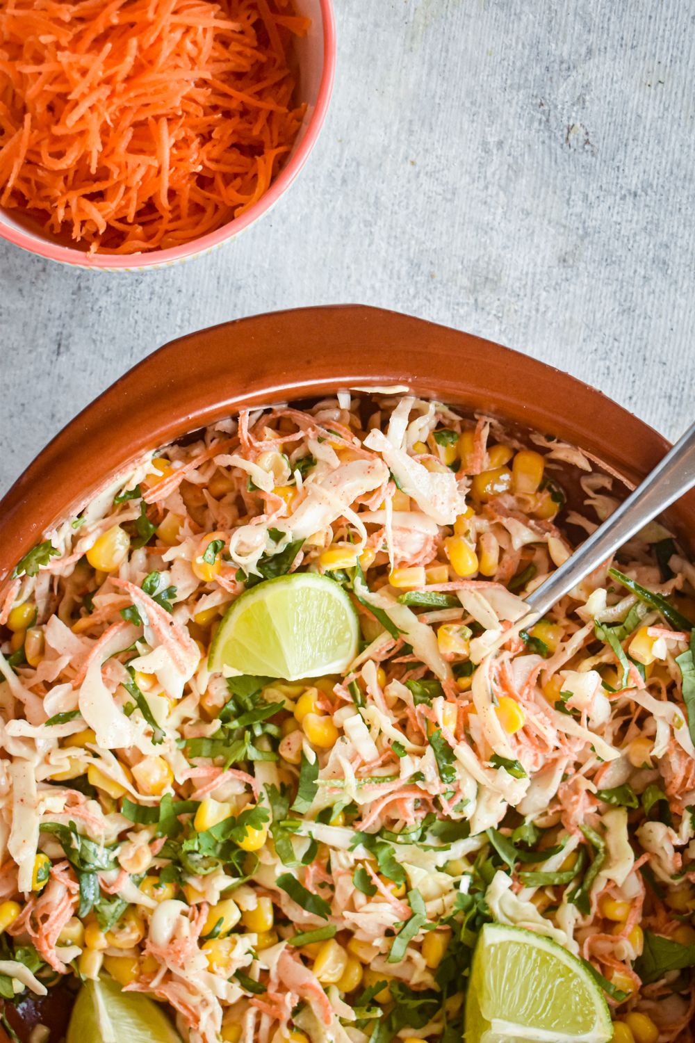 Spicy cabbage slaw with corn and carrots in a wooden bowl with creamy dressing and a spoon.