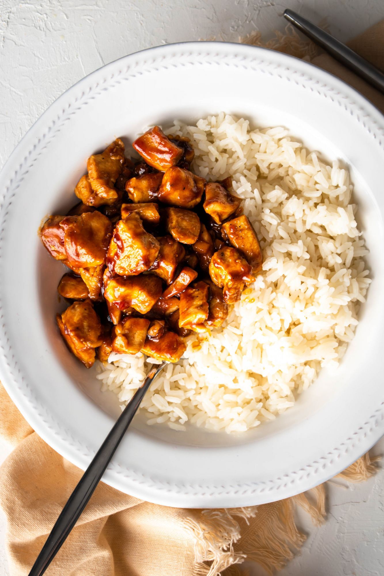 Hoisin chicken breast served with white rice in a bowl with a beige napkin on the side.